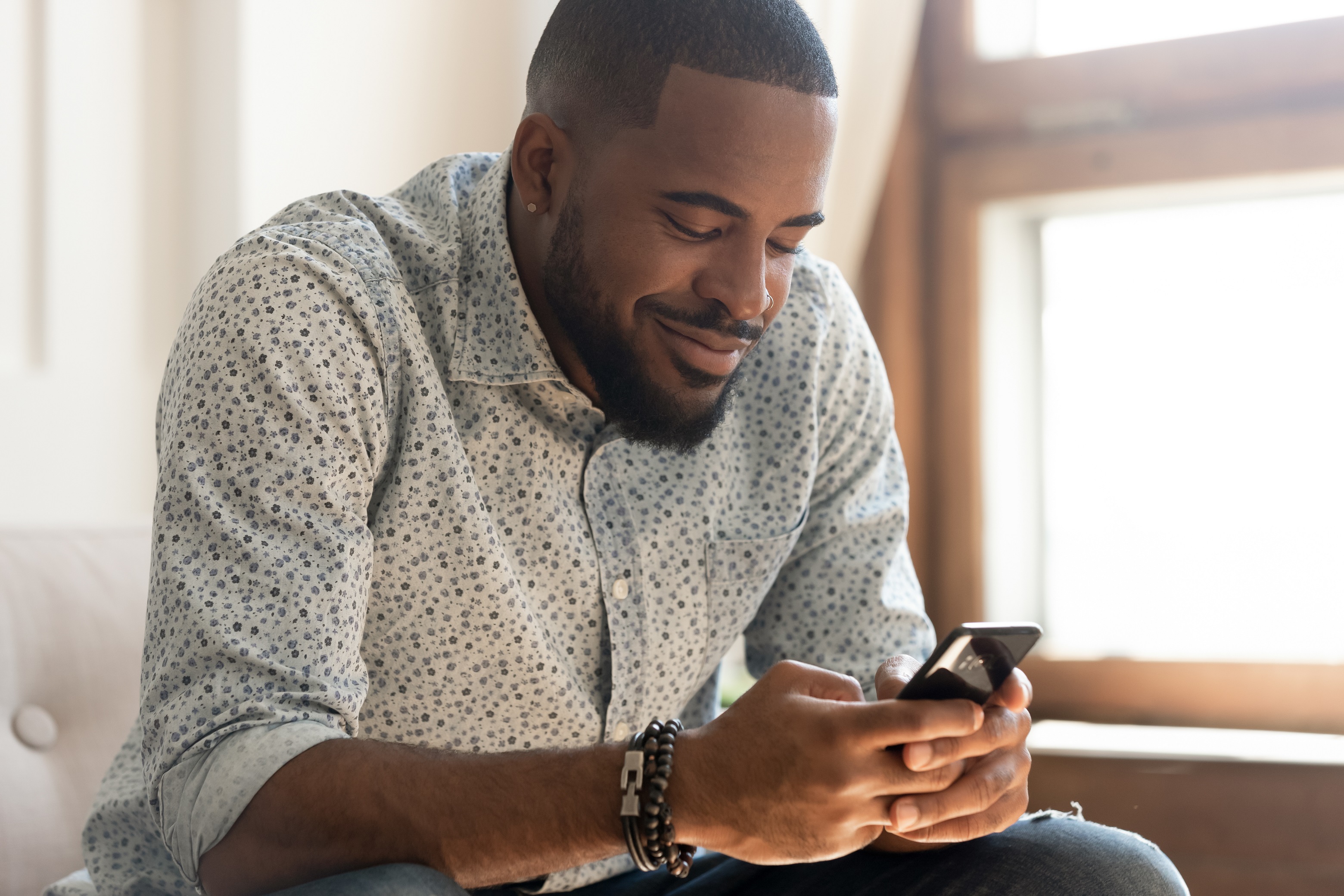 Smiling african American man feel happy texting on smartphone